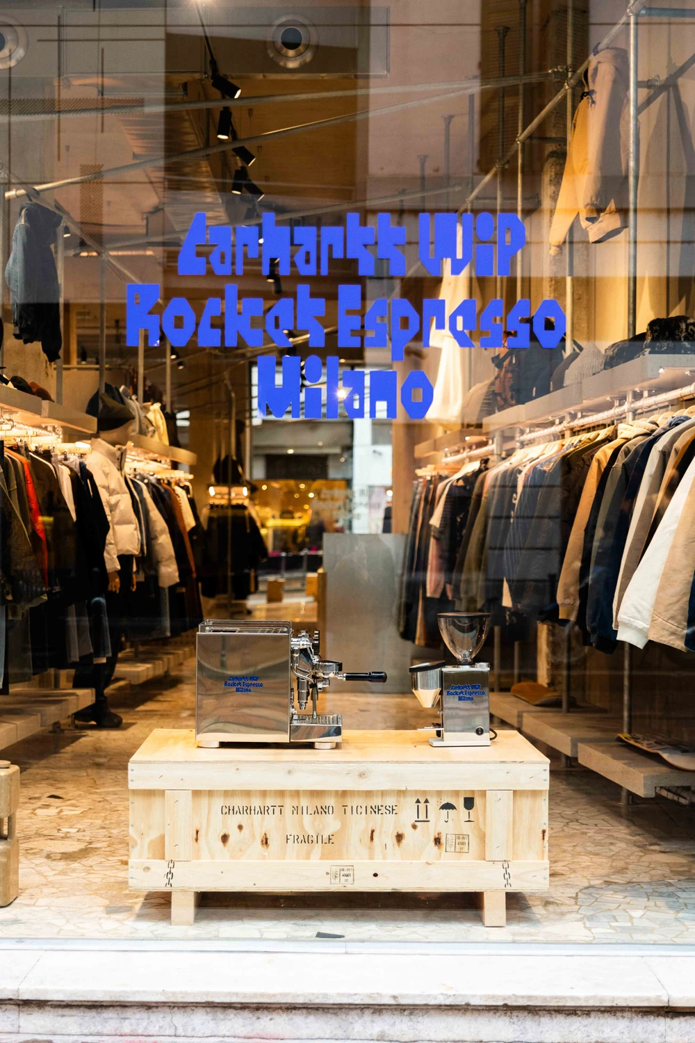 Carhartt WIP × Rocket Espresso window display in Milan with the silver machine and grinder on a wooden crate