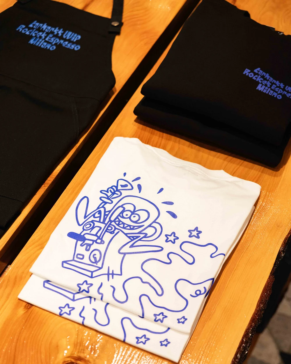 Collaboration aprons and shirts with blue Carhartt WIP × Rocket Espresso graphics