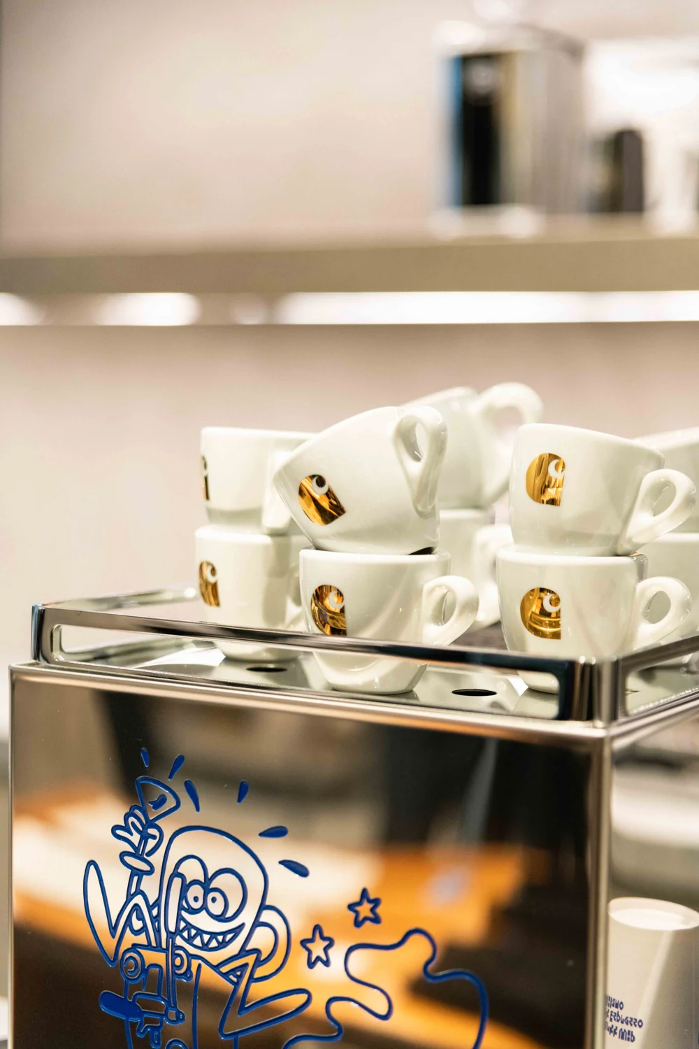 White espresso cups with gold Carhartt logos on the polished silver machine