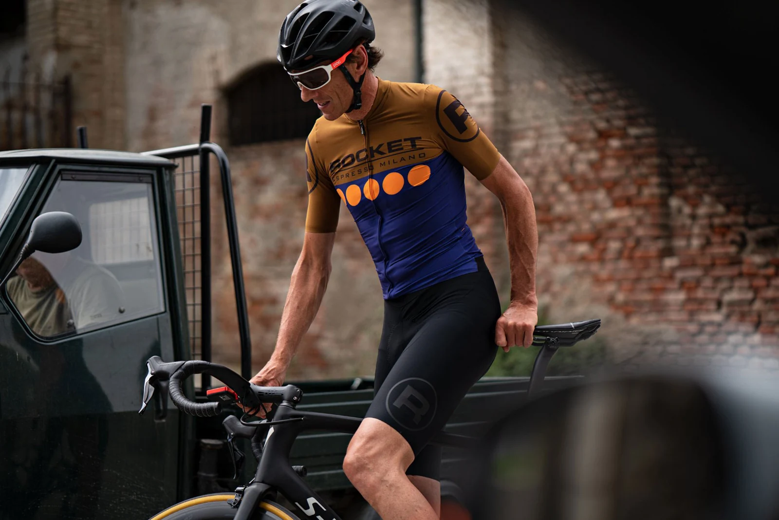 Cyclist wearing the navy and ochre Rocket jersey and bib shorts beside an Ape van