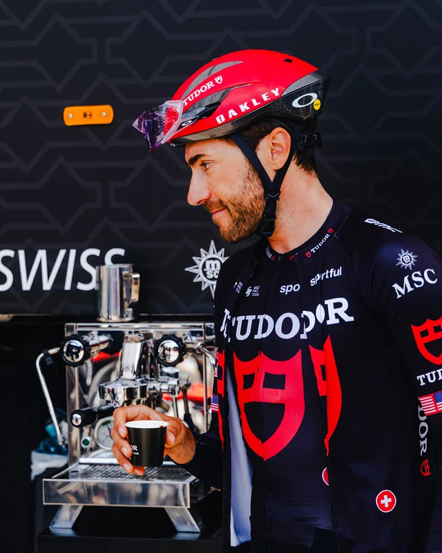 Larry Warbasse in Tudor Pro Cycling kit holding an espresso beside a Rocket machine at the 2026 Giro d’Italia